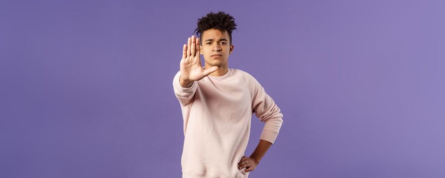 Portrait of confident serious-looking determined young man trying to prevent something, pull hand in stop gesture, look camera assertive, prohibit, give warning or forbid something