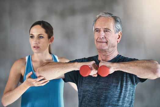 Maintaining muscle mass with regular exercise. a senior man using weights with the help of a physical therapist.