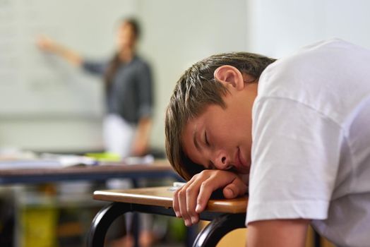 This class is a snoozefest. a young schoolboy sleeping on his desk in class.