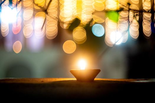 lone earthenware oil lamp diya set against colorful bokeh balls showing the lighting and decoration during the hindu festival of diwali showing a serene peaceful vision in the night
