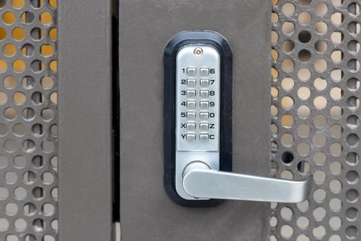Locked private metal security gate door with push button combination lock system keypad with metallic silver doorknob handle.