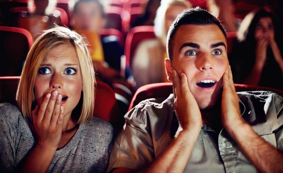 Couple watch a scary, horror or thriller movie in a cinema together and are shocked, wow or surprised. Man and woman in theatre on a date with omgand scared emotion or fear while watching a film