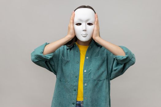 Unknown woman holding white mask, standing covering face, multiple personality disorder.