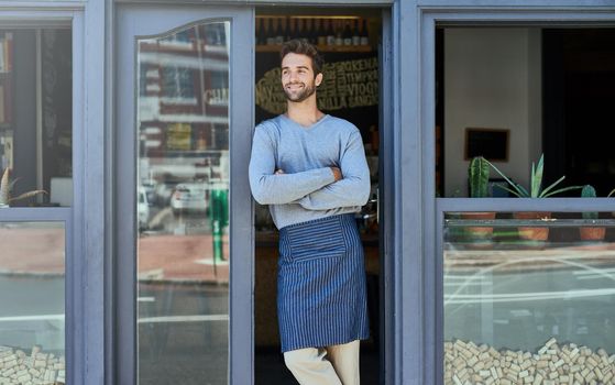 The anticipation feels great. a handsome and confident young man standing in the doorway of his business.