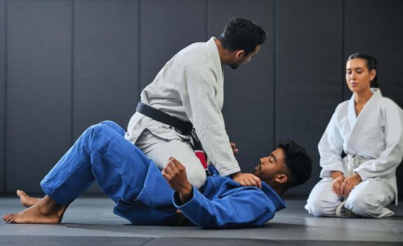 Karate, fitness and martial arts instructor teaching a lesson on fighting and defense training at a gym or indoor center. Diverse sporty student learning how to be safe in an attack with tough coach