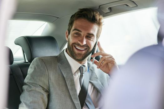 Traveling in business style. a handsome young businessman talking on a cellphone in the back seat of a car.