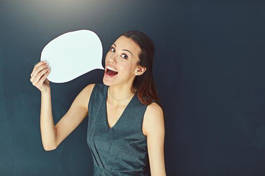 Speak your mind. Portrait of a young woman posing with a speech bubble against a gray background.