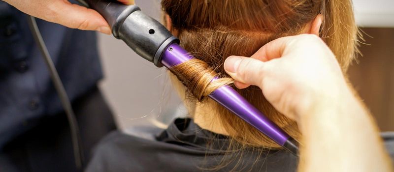 Close up of hairstylist's hands using a curling iron for hair curls in a beauty salon.