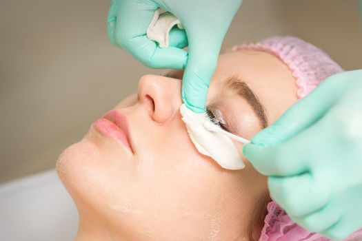Young woman receiving eyelash removal procedure and removes mascara with a cotton swab and stick in a beauty salon.