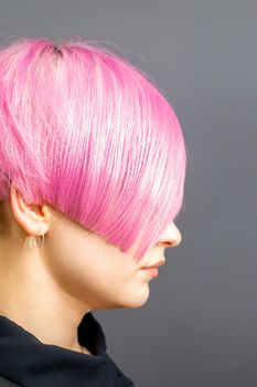 Profile portrait of a young caucasian woman with pink bob haircut isolated on a gray background.