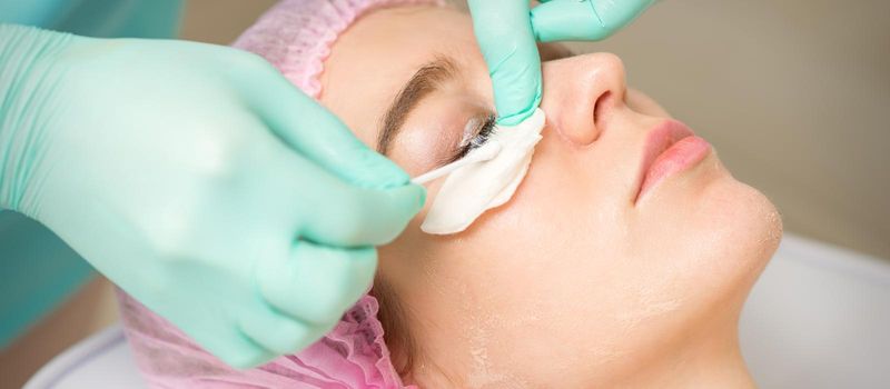 Young woman receiving eyelash removal procedure and removes mascara with a cotton swab and stick in a beauty salon.