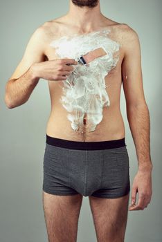 Body hair be gone. Studio shot of a man shaving his chest hair against a gray background.