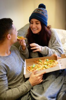 Eat up. a happy young couple eating pizza while relaxing on the sofa at home.