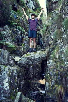 Conquering the great outdoors. a young man raising his hands while exploring a hiking trail alone.
