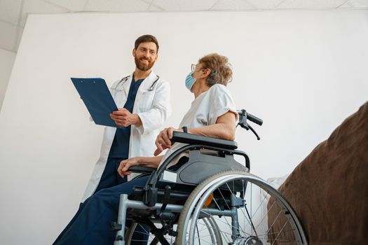 Doctor inuniform explaining to a sick patient in a wheelchair the details of treatment