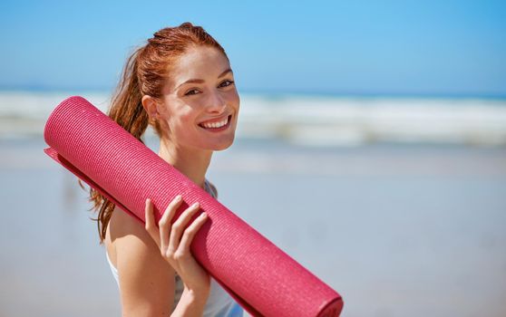 Yoga is about showing up to your mat. a young woman posing with her yoga mat on the beach.