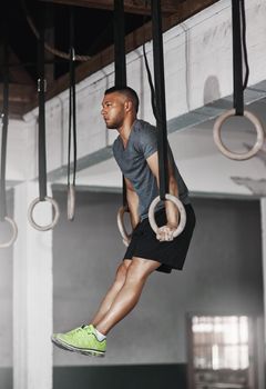 Lifting himself higher. Full length shot of a young man working out on the gymnastics rings.
