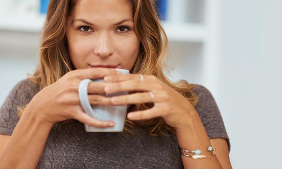 Cozying up to a cup of coffee. Portrait of a young woman enjoying a warm beverage at home.