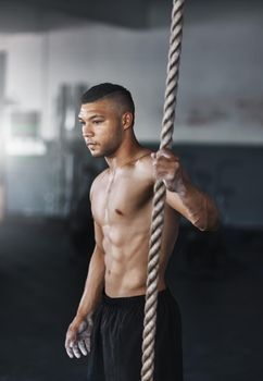 Fitness is a battle against yourself. a young man climbing a rope at the gym.
