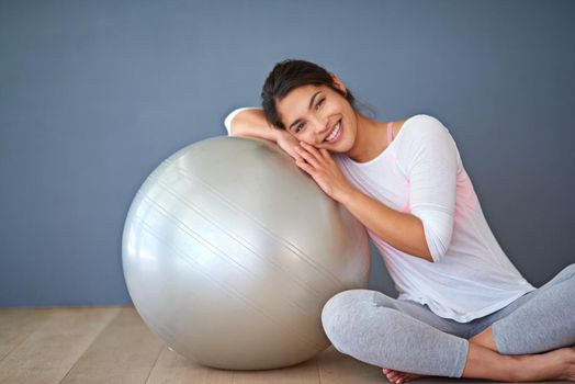 The ball that gets me on the ball. a sporty young woman leaning on a pilates ball against a grey background.