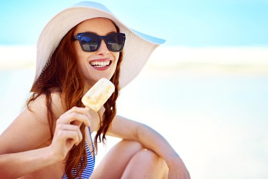 Summer is a time for ice cream. Portrait of a beautiful young woman eating an ice cream at the beach.