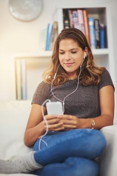 Downloading her weekend playlist. a young woman listening to music on her phone at home.