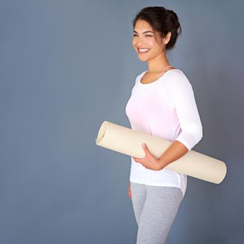 All it takes is all youve got. a sporty young woman holding her yoga mat against a grey background.