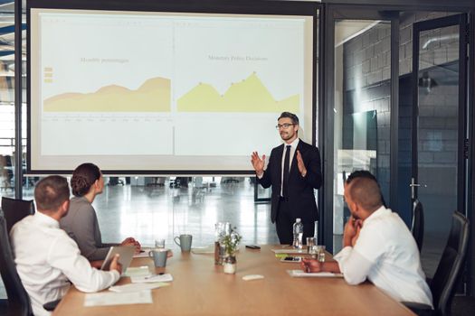 Talking profit and loss in the boardroom. an executive giving a presentation on a projection screen to a group of colleagues in a boardroom.