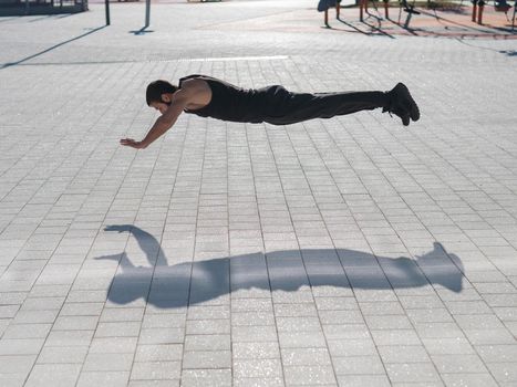 A man in black sportswear jumps doing push-ups in the park.