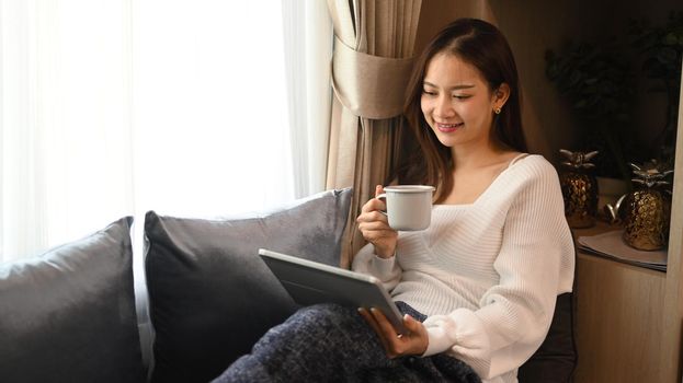 Happy young woman surfing internet on digital tablet in cozy winter or autumn weekend