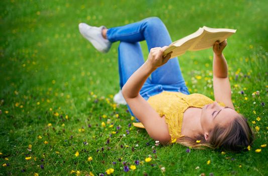 Escape with a good book. a carefree young woman relaxing in a field of grass with a book.