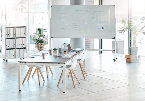 Boardroom, meeting or empty conference room with whiteboard, chairs and table interior of modern creative office space. Marketing data and charts for a business presentation, discussion of briefing