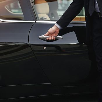 Top class transportation. a well dressed man opening a car door.