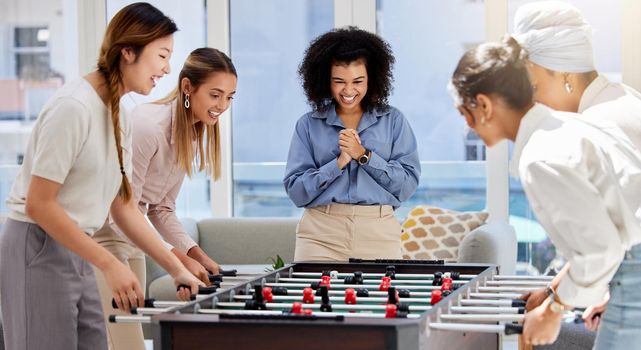 Team building, break and business women playing game in office lounge room having fun and bonding together. Trendy, cool and diversity of creative staff with fun mini table football match activity