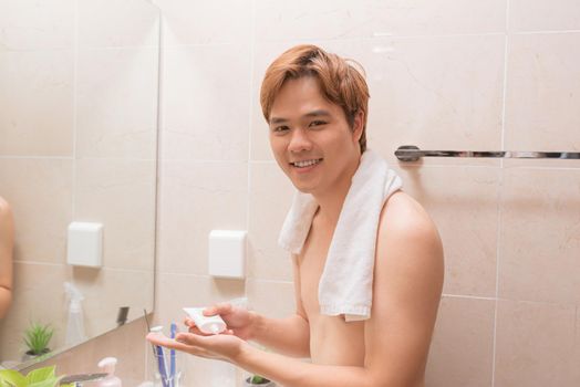 Portrait of beautiful smiling healthy guy applying foam for washing on his face.