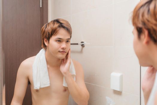 Young man looking in mirror and checking his stubble in bathroom
