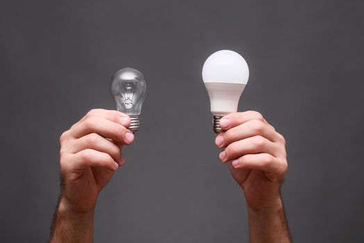incandescent lamp and led economical lamp in the hands on a gray background. 