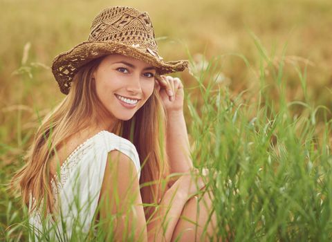 Happy girls are the prettiest. a young woman sitting in a field in the countryside.