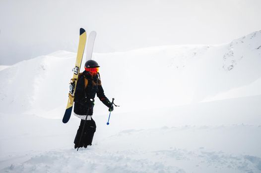 Young woman with ski equipment and sticks are climbing a snowy mountain, backcountry. Foggy sky and snowy mountain in the background