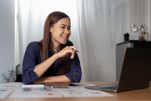 Cheerful woman freelancer working online on laptop, sitting at desk at home, looking at screen.