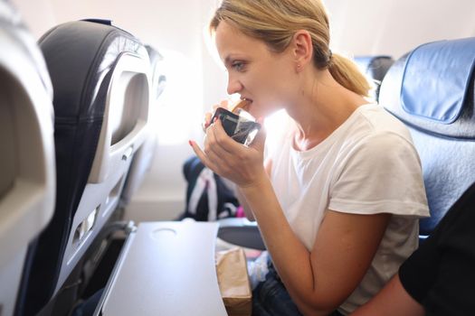 Woman eats juicy tasty sandwich in cabin of an airplane
