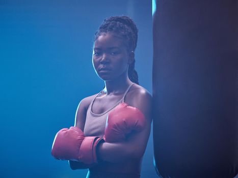 Fitness, boxer and gym of a black woman in sports professional for strength and motivation. Portrait of a African female in serious and confident boxing at health club standing by punching bag