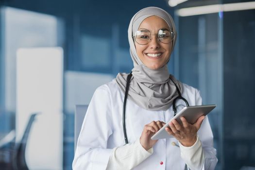 Young beautiful woman muslim doctor in hijab smiling and looking at camera working with tablet