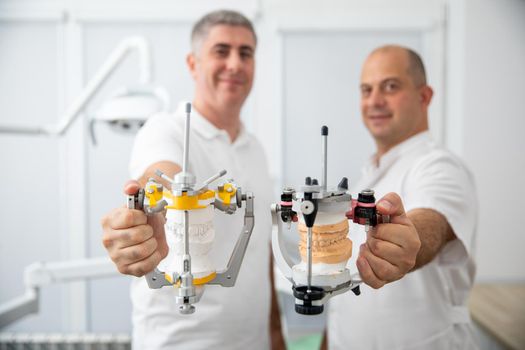 Two male dentists holding dental articulators in dental clinic