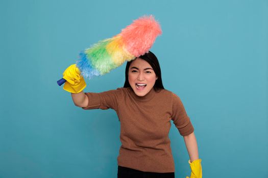 Angry energetic young asian houseworker holding colorful dust brush