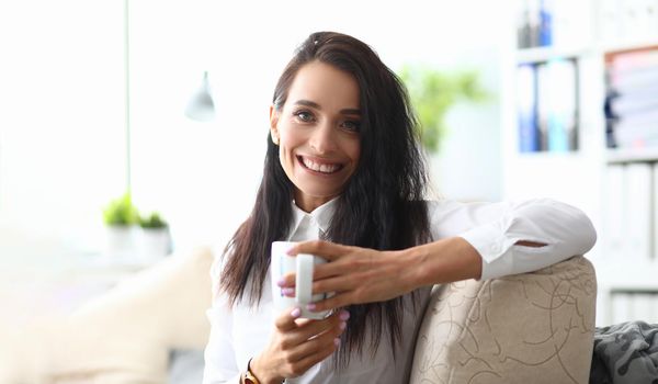 Portrait of smiling minded successful employee business woman in white shirt with cup