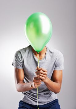 Let go and set yourself free. a man covering his face with a balloon over a gray background.