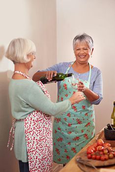 And a splash for us. two senior woman drinking wine while cooking.