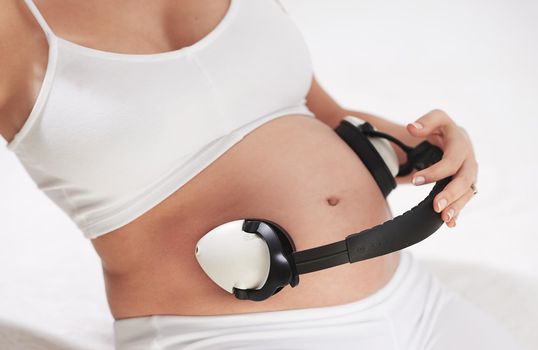 Soothing tunes for a growing tummy. a pregnant woman holding headphones around her belly.