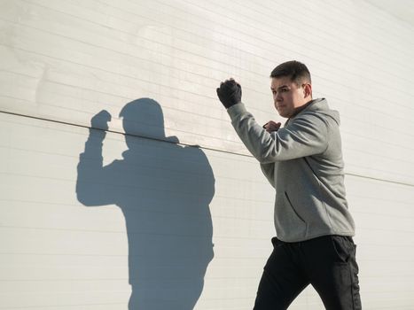 Caucasian man in hoodie is training boxing outdoors.